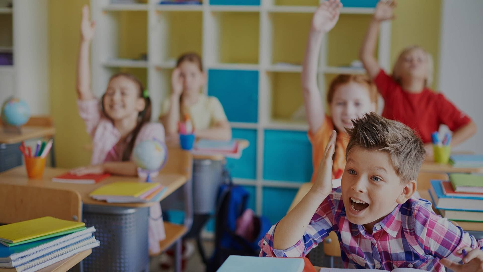 Happy children in the classroom raising their hands